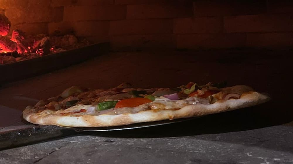 En nybakad pizza på spaden i Donna Ginas vedugn
